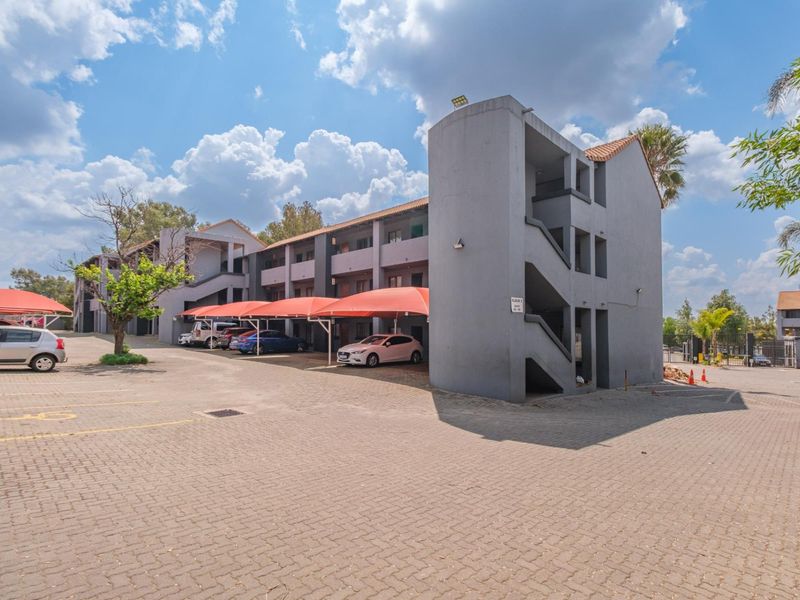 Exterior view of a multi-story apartment complex featuring paved parking areas and covered parking bays.