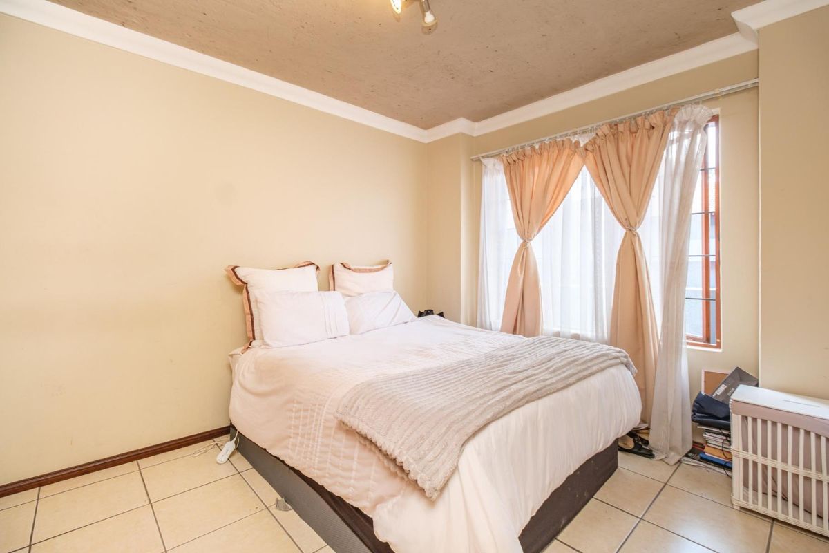 A bedroom featuring tiled flooring, ceiling cornice, and a window with curtains. The room shows signs of wear on the ceiling and floor tiles.
