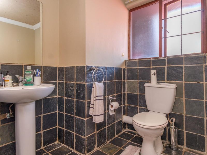 A functional bathroom featuring dark slate wall and floor tiling, a white pedestal sink, and a standard toilet with a window for natural light.