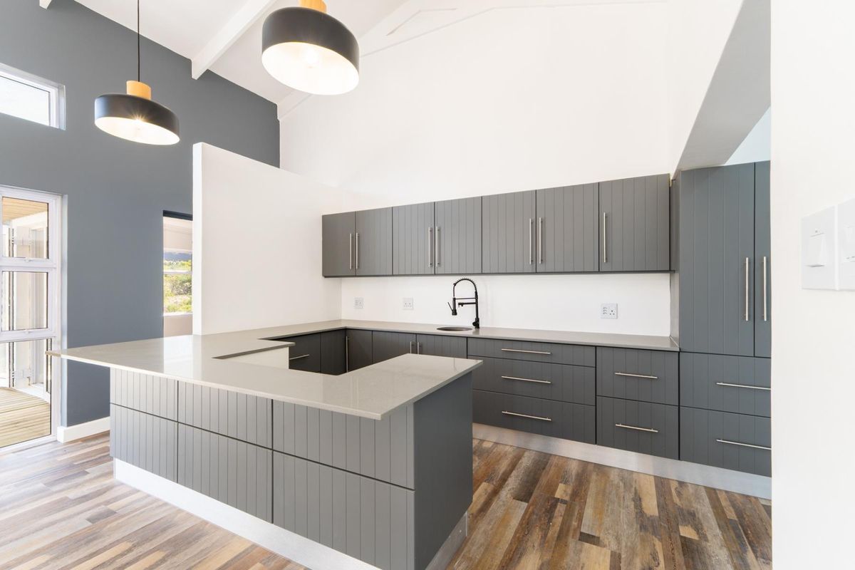 Modern kitchen featuring dark grey shaker-style cabinetry, quartz countertops, an undermount sink with a gooseneck faucet, and high vaulted ceilings.