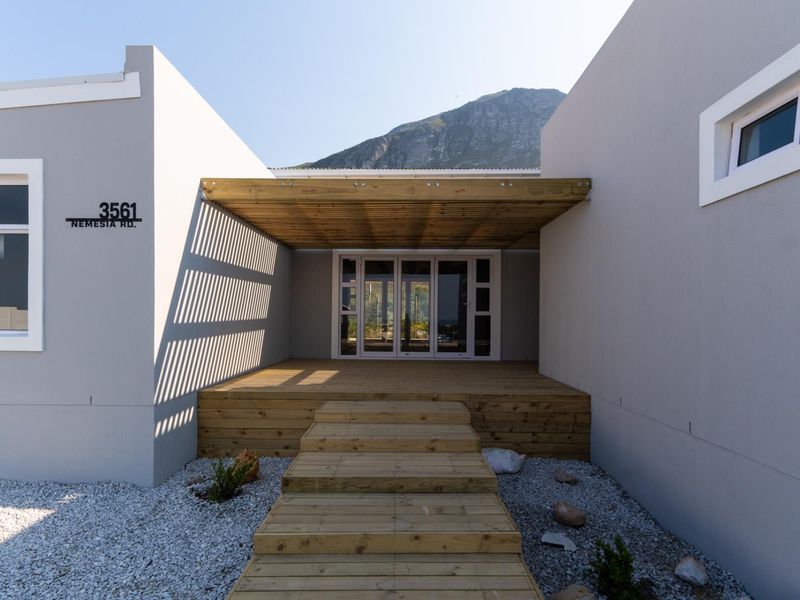 Modern front entrance featuring timber decking, a matching pergola, and glass sliding doors, set against a mountain backdrop.