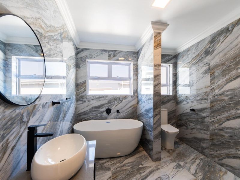 Modern luxury bathroom featuring floor-to-ceiling marble-look tiling, a sleek freestanding bathtub, vessel sink, and high-end black fixtures.