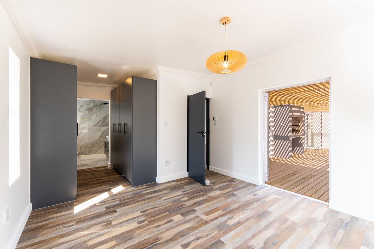 Bright bedroom featuring modern laminate flooring, built-in cupboards, and direct access to an outdoor patio area.