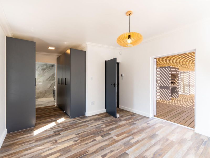 Bright bedroom featuring modern laminate flooring, built-in cupboards, and direct access to an outdoor patio area.