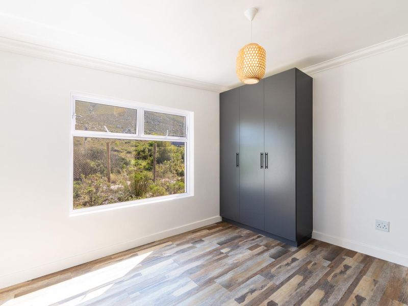 A bright, modern bedroom featuring durable laminate flooring, a sleek dark grey built-in wardrobe, and a large window with natural light.
