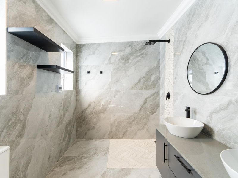 Modern bathroom featuring a spacious walk-in shower with rain head, double vanity with vessel sinks, and elegant grey marble-look tiling throughout.