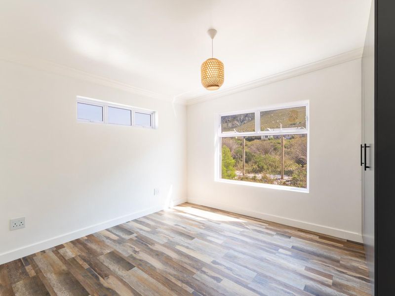 A bright, empty bedroom featuring modern laminate flooring, built-in wardrobe, and large windows with natural light.