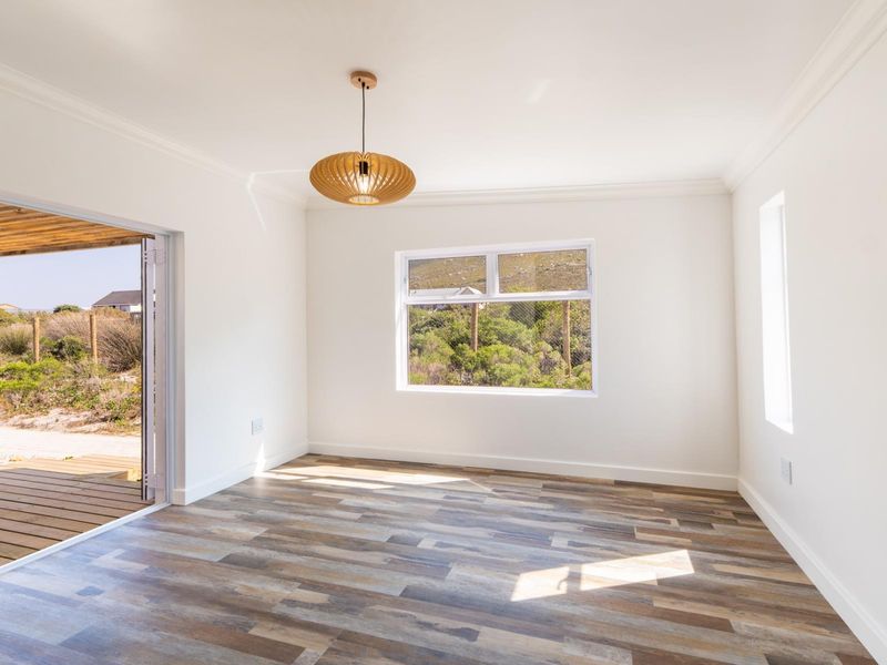 A bright, empty living room featuring modern laminate flooring, crisp white walls, and a sliding glass door leading to an outdoor deck.