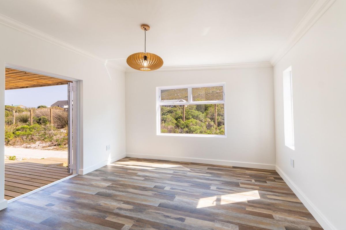 A bright, empty living room featuring modern laminate flooring, crisp white walls, and a sliding glass door leading to an outdoor deck.