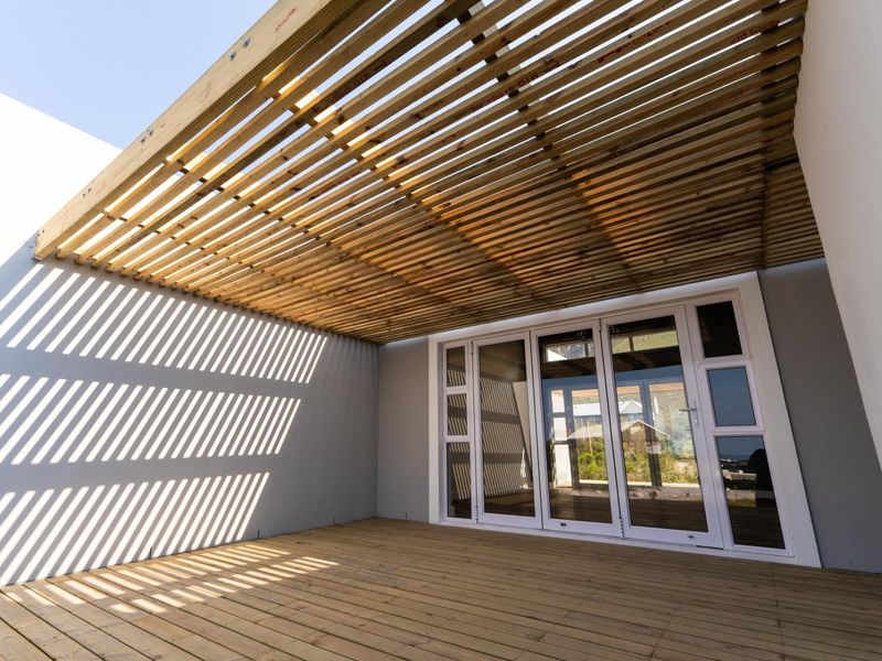 A modern outdoor patio featuring timber decking and a slatted timber pergola, providing a seamless transition to the interior through large glass sliding doors.