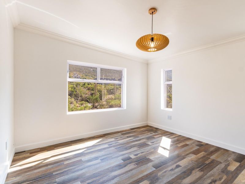 A bright, empty bedroom featuring modern laminate flooring, crisp white walls, decorative cornice, and large windows providing natural light and scenic views.