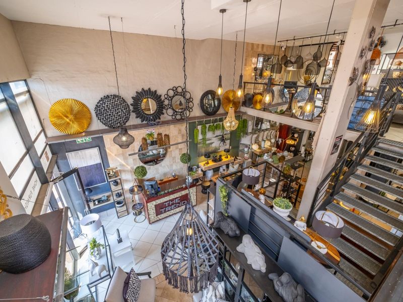 A spacious multi-level retail showroom featuring high ceilings, a mezzanine level, a metal staircase, and large windows providing ample natural light.