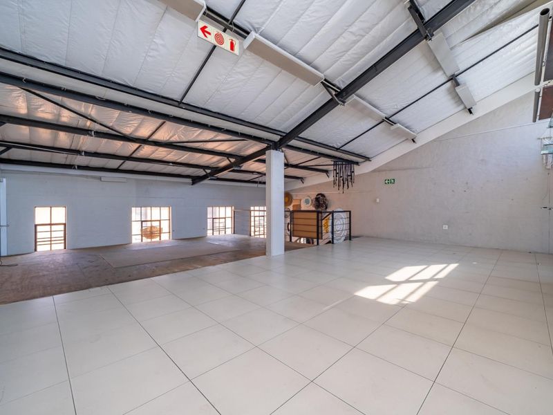 Spacious open-plan retail or office area featuring high exposed steel roof trusses, insulated ceiling, tiled flooring, and large industrial-style windows providing natural light.