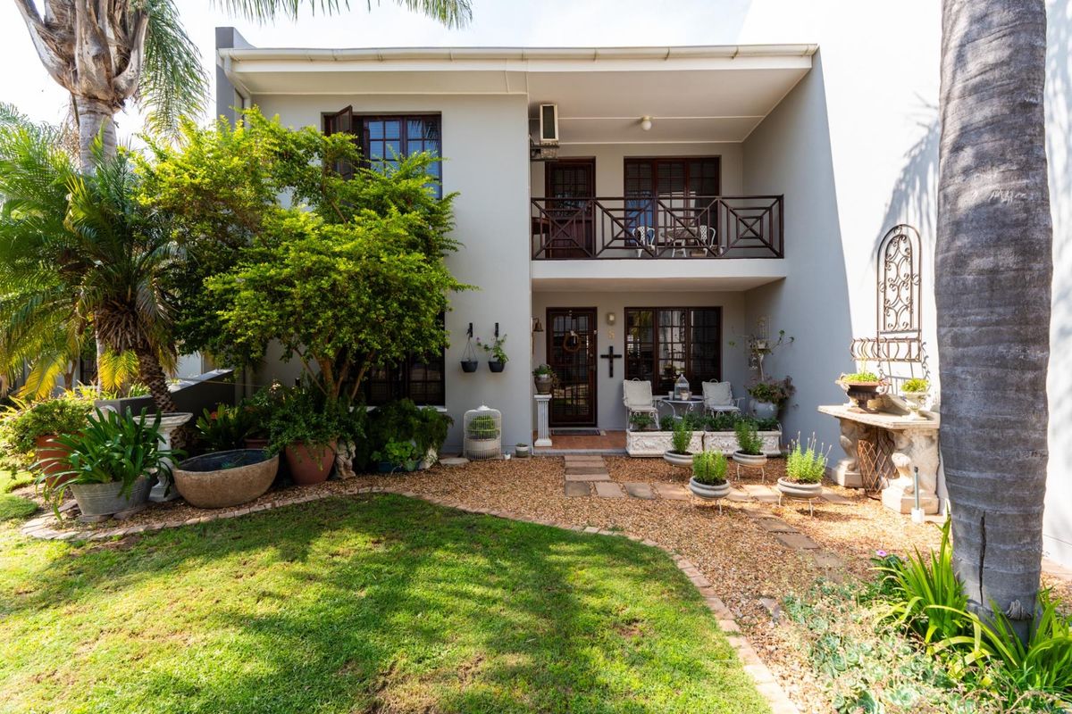 Rear view of a two-story townhouse featuring a ground floor patio, upper balcony with timber railings, and a landscaped garden with a stone path.