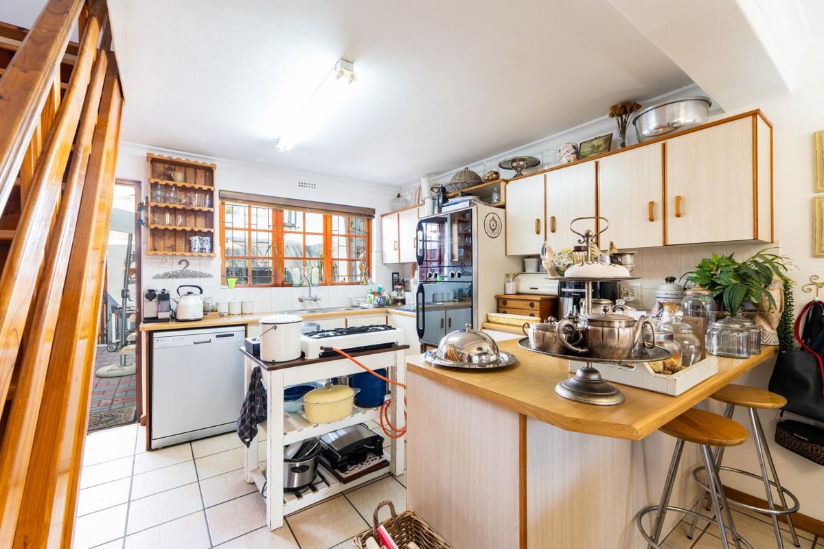 A functional kitchen featuring built-in cabinetry, laminate countertops, a double sink, and tiled flooring, with an adjacent staircase leading to the upper level.