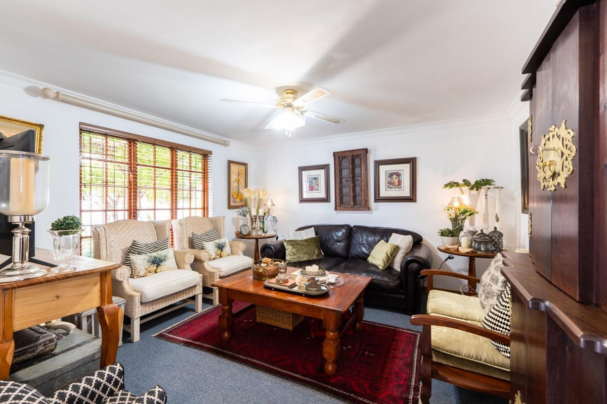 A comfortable living room featuring a ceiling fan and large windows with wooden blinds, offering a bright and inviting space for relaxation.