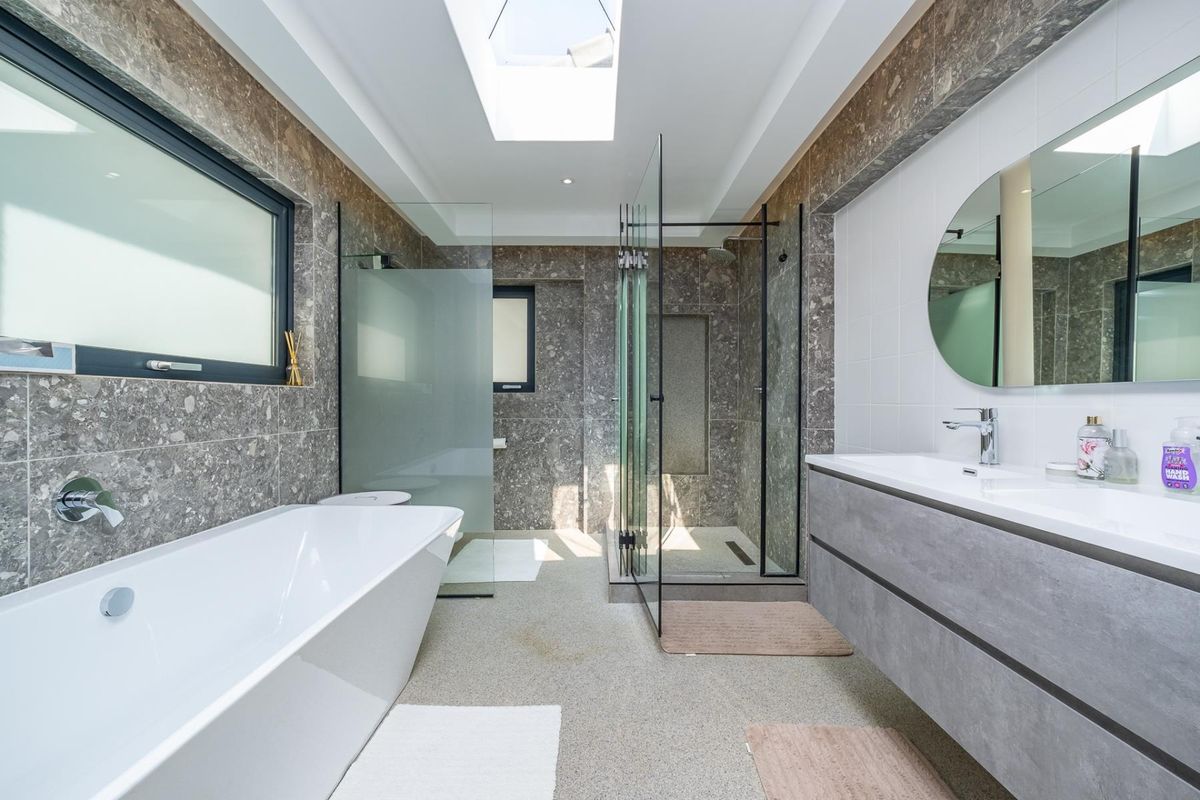 Modern, high-end bathroom featuring a sleek freestanding bathtub, a spacious walk-in shower with glass enclosure, double vanity, and a bright skylight.
