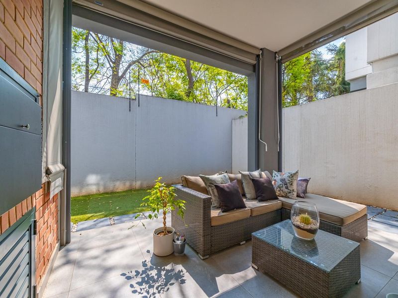 A covered patio area featuring tiled flooring, a built-in braai, and retractable outdoor blinds, opening onto a private garden space.