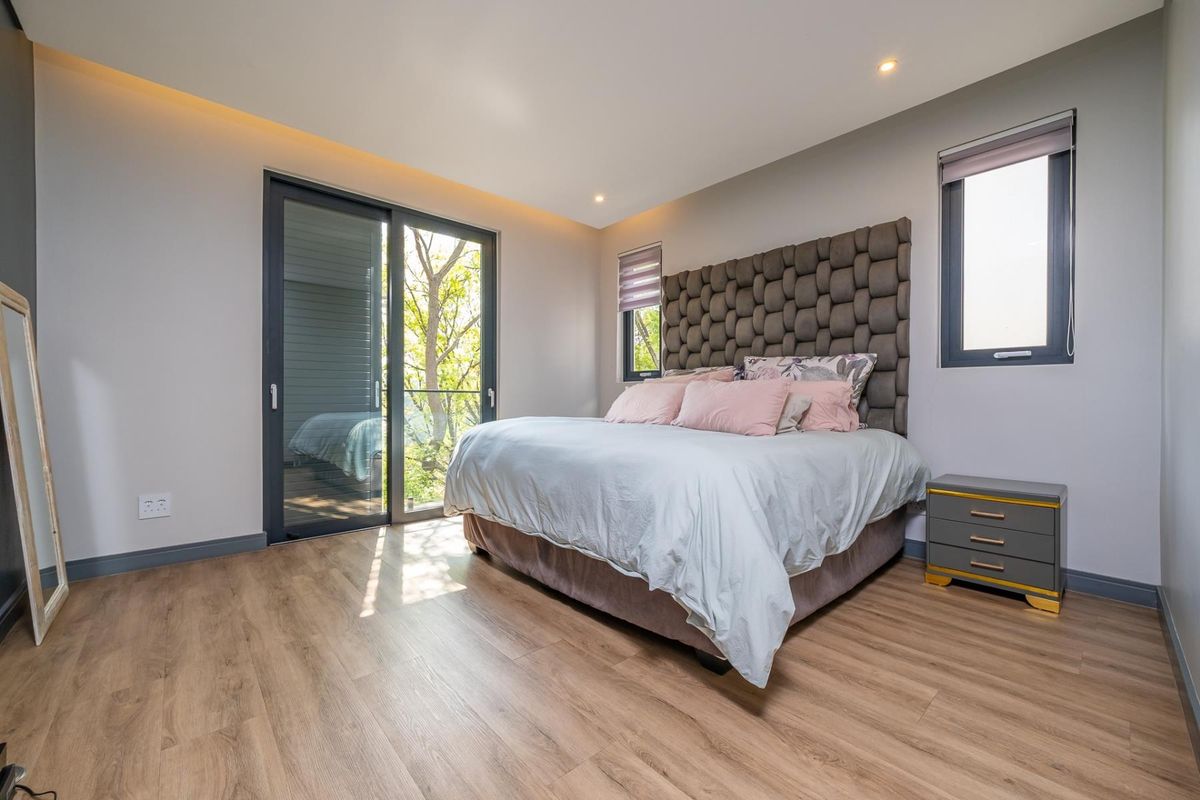Modern bedroom featuring laminate flooring, recessed downlighting, cove lighting, and a sliding glass door providing access to an outdoor area.
