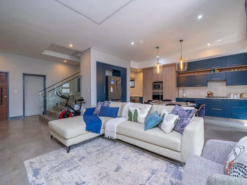 Modern open-plan living area featuring a contemporary kitchen with dark blue cabinetry, integrated appliances, and a seamless transition to the staircase with glass balustrade.
