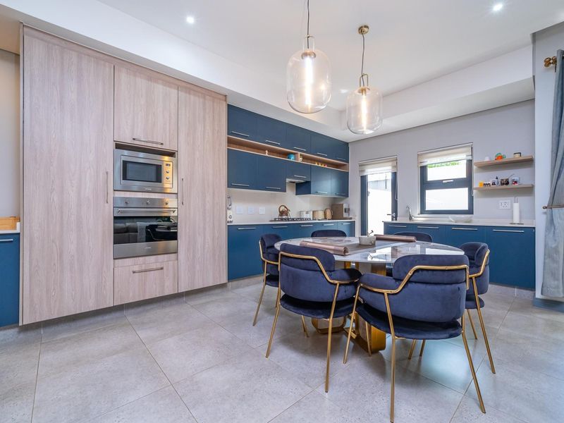 Modern open-plan kitchen featuring blue and wood-grain cabinetry, stone countertops, integrated appliances, and stylish pendant lighting, seamlessly flowing into the dining area.