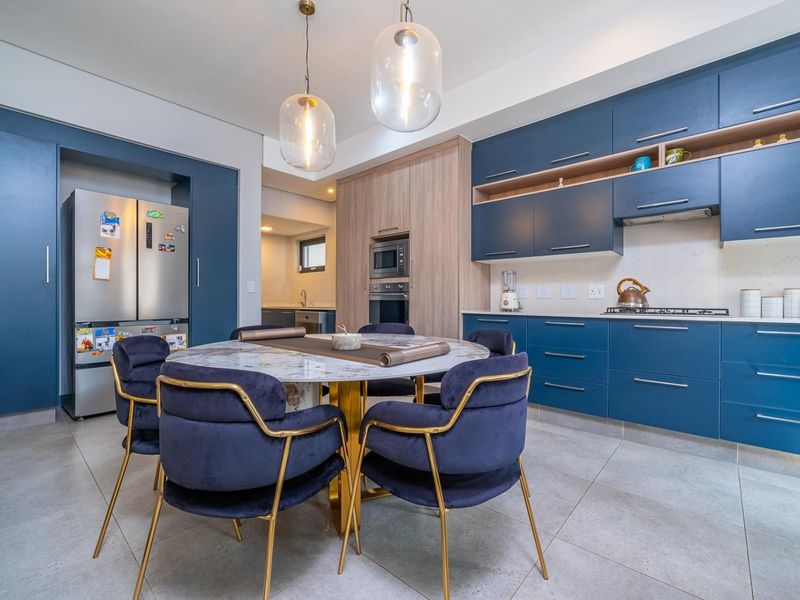 Modern open-plan kitchen and dining area featuring sleek blue cabinetry, integrated appliances, stone countertops, and contemporary pendant lighting.