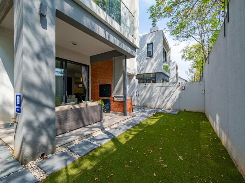 Covered patio area featuring a built-in braai, sliding door access to the interior, and a private garden space with artificial lawn and stone pavers.