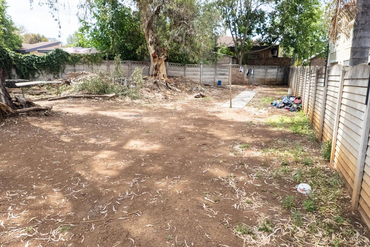 A spacious backyard area featuring mature trees and precast concrete boundary walls, currently requiring landscaping and clearing to reach its full potential.