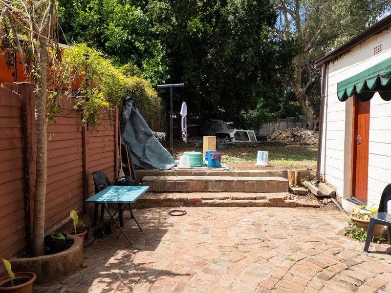 A rear outdoor area featuring a brick-paved patio, stone steps leading to a garden space, and a side wall with a protective awning.