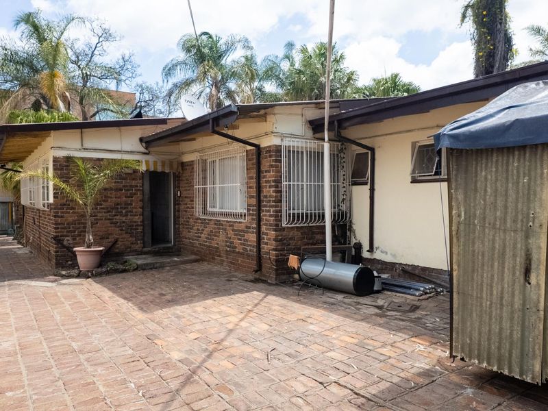 Rear exterior view of the property featuring a brick facade, paved courtyard area, and security bars on the windows.
