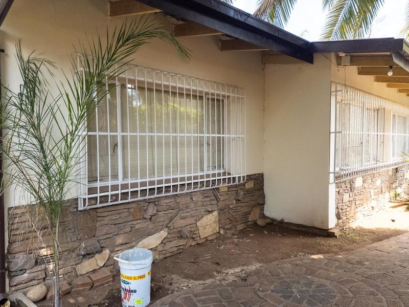 Rear exterior view of the house featuring stone cladding, security bars on windows, and a paved patio area with exposed roof rafters.