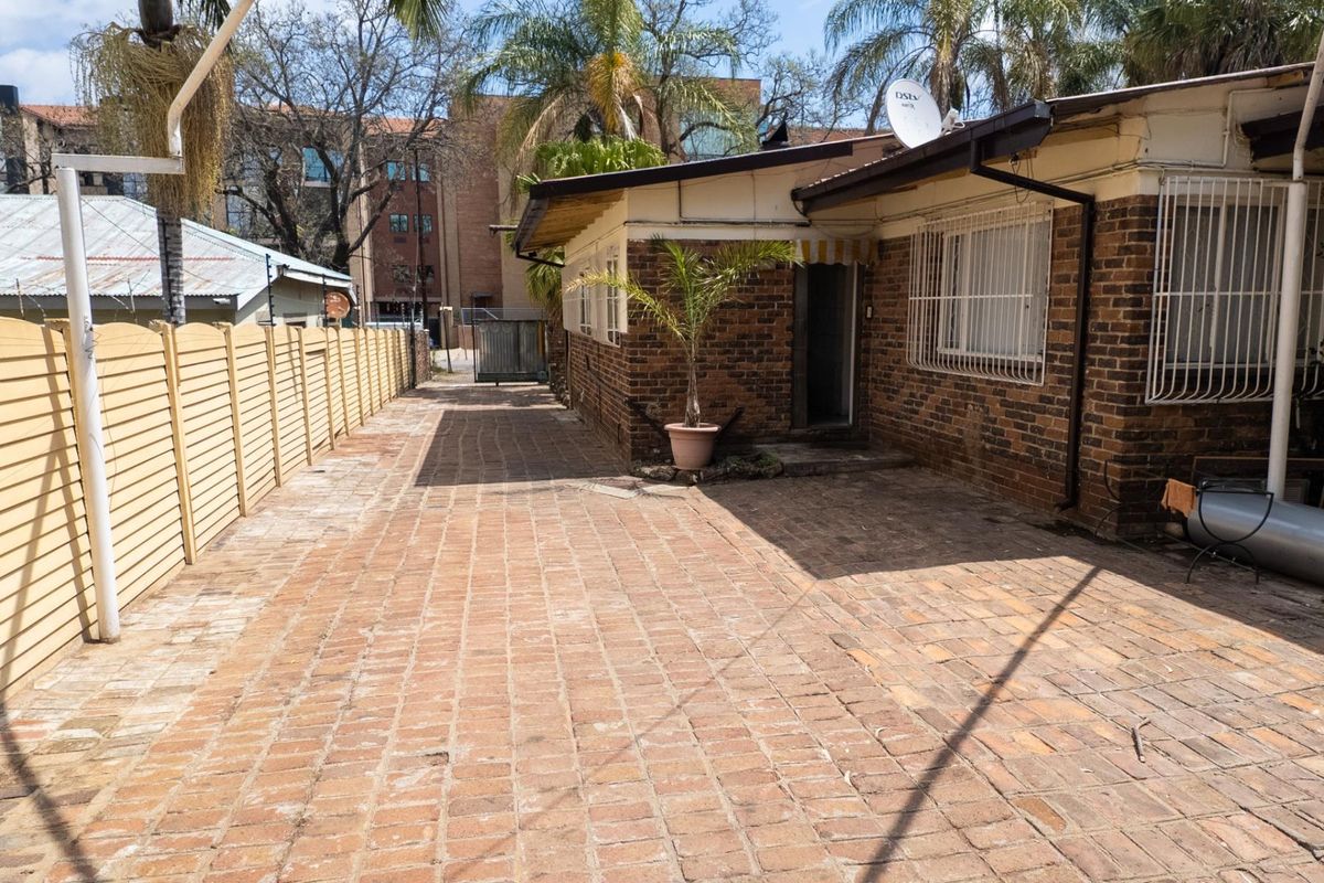 Rear exterior view of the property featuring brick facade, paved courtyard area, and security window bars.