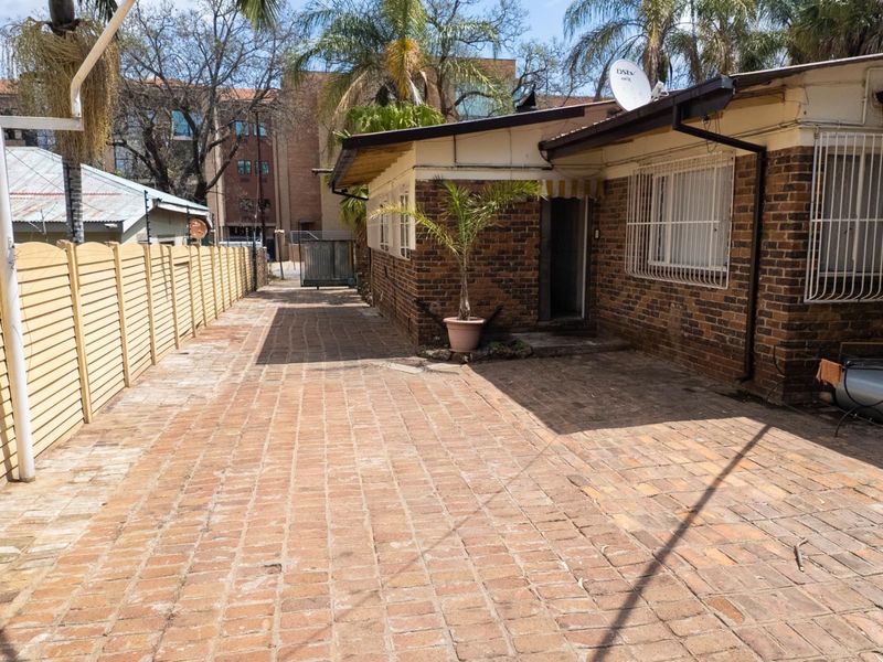 Rear exterior view of the property featuring brick facade, paved courtyard area, and security window bars.