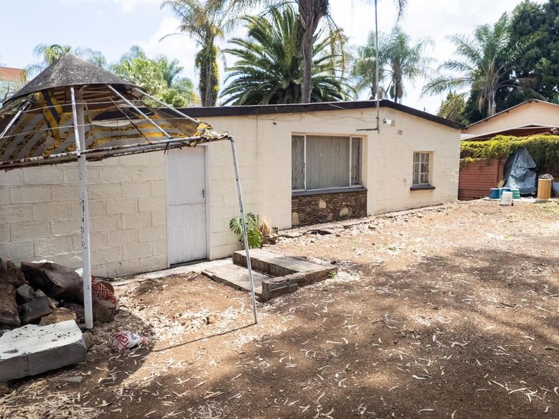 Rear view of the property showing a masonry structure with stone detailing, requiring significant exterior maintenance and landscaping.