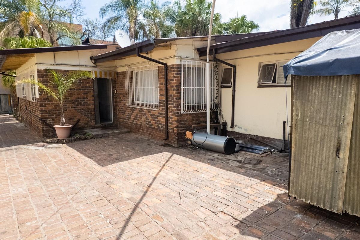 Rear exterior view of the property featuring brick paving, security bars on windows, and exposed brickwork walls.