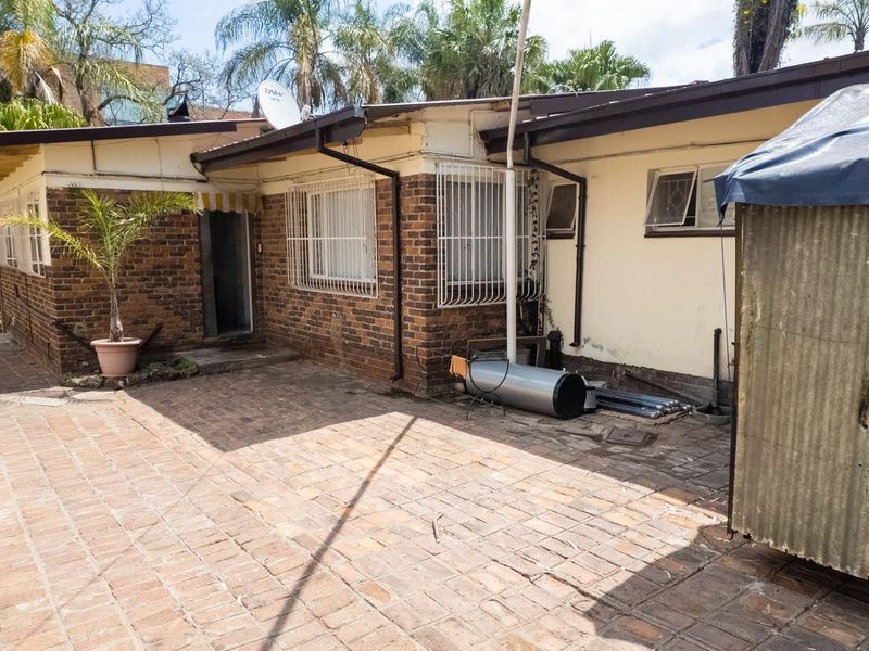 Rear exterior view of the property featuring brick paving, security bars on windows, and exposed brickwork walls.