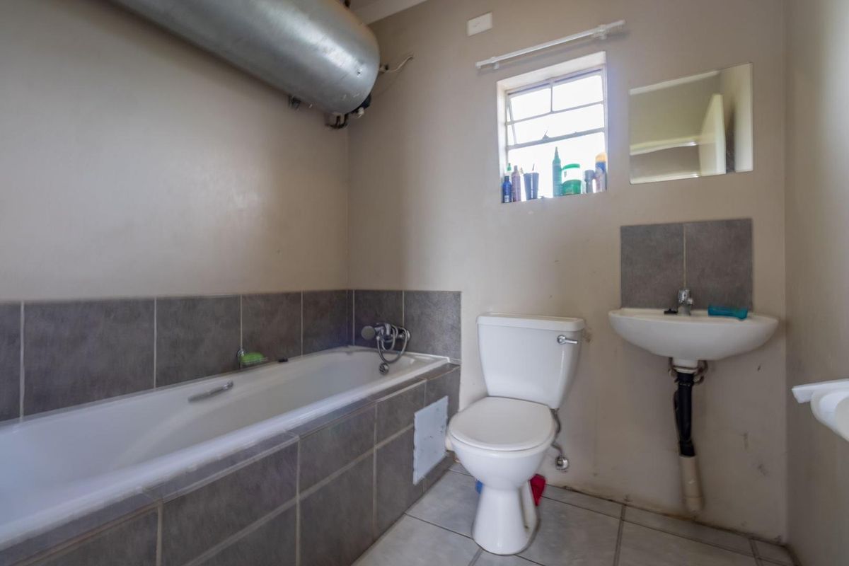 A functional bathroom featuring a bathtub, pedestal basin, and toilet, with tiled finishes and an exposed geyser unit.