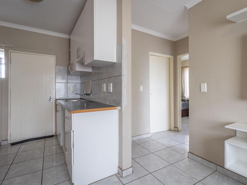 Compact kitchen area featuring white cabinetry, tiled backsplash, and tiled flooring, leading into a hallway with access to adjacent rooms.