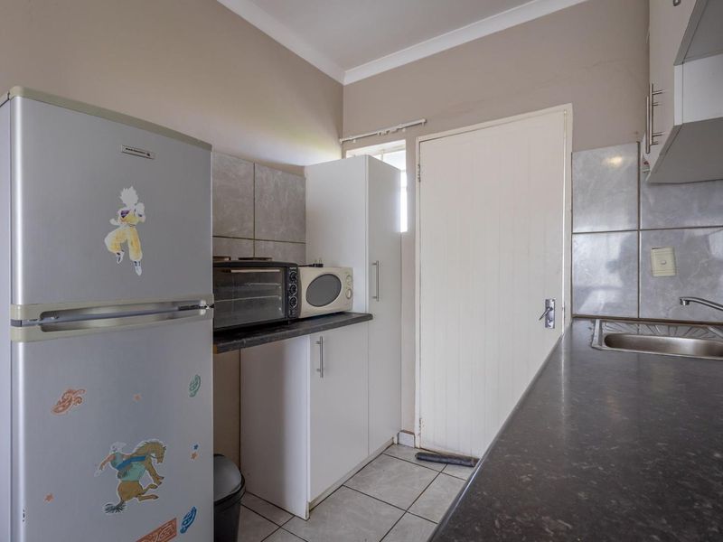 Compact kitchen featuring laminate countertops, stainless steel sink, tiled backsplash, and built-in cabinetry with tiled flooring.