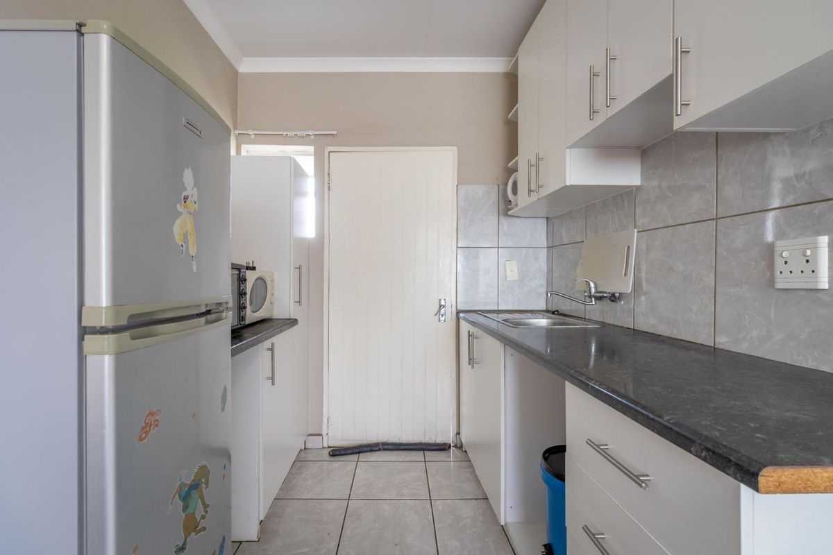 A functional kitchen featuring white cabinetry, dark laminate countertops, tiled backsplash, and tiled flooring, providing a practical workspace for daily meal preparation.