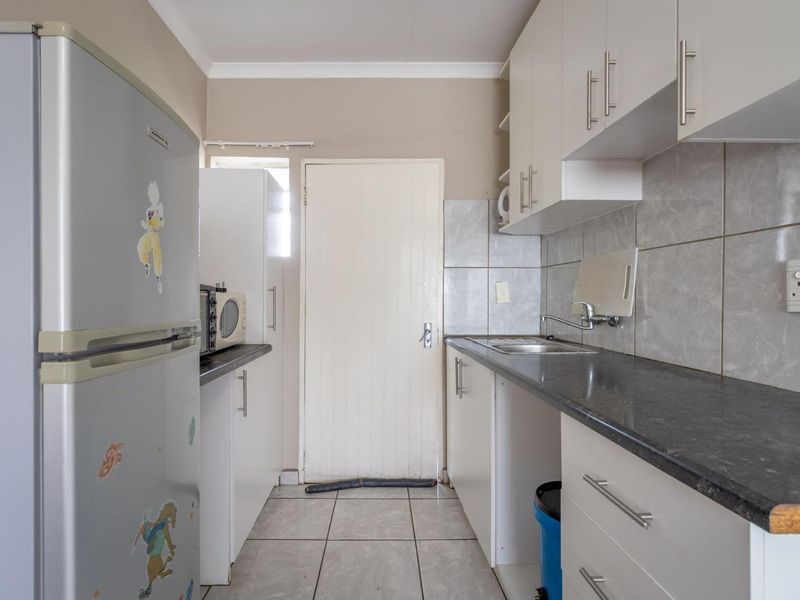 A functional kitchen featuring white cabinetry, dark laminate countertops, tiled backsplash, and tiled flooring, providing a practical workspace for daily meal preparation.