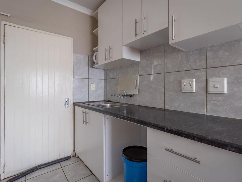 A functional kitchen area featuring white built-in cabinetry, dark laminate countertops, a stainless steel sink, and neutral tiled backsplash and flooring.
