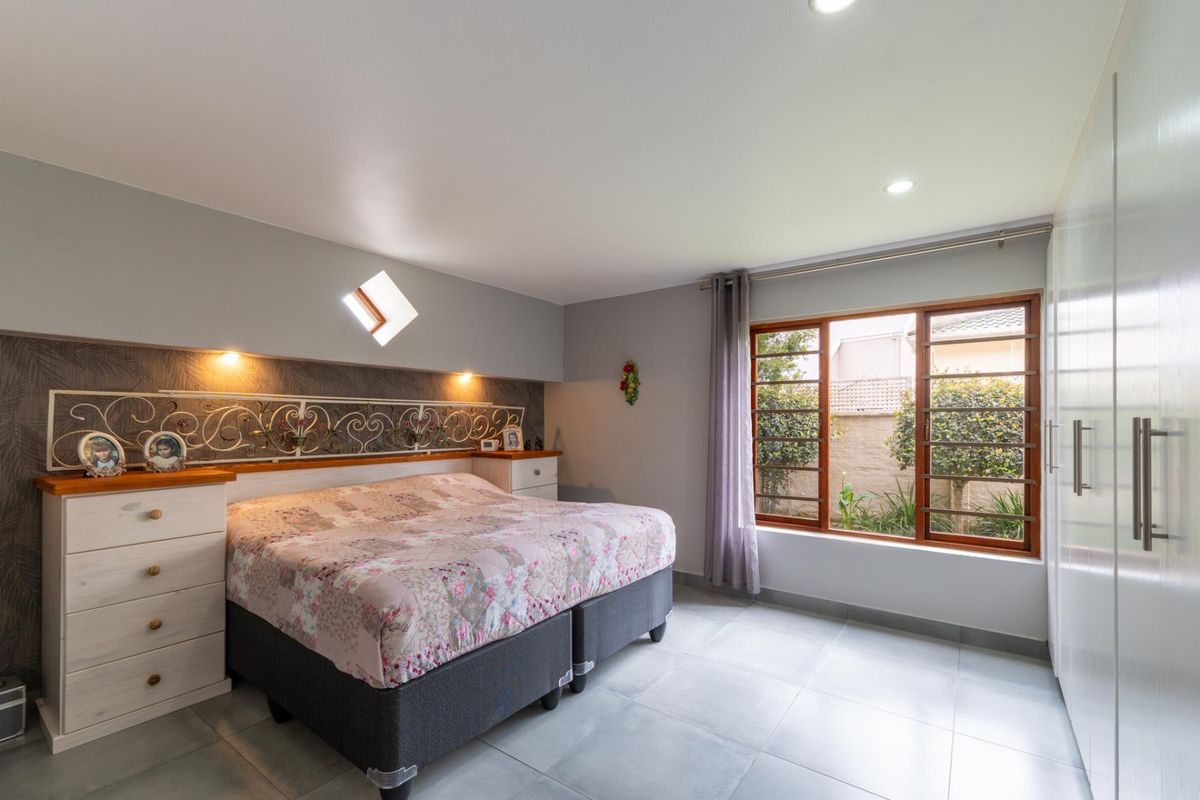 A well-maintained bedroom featuring tiled flooring, built-in cupboards, recessed lighting, and a unique diamond-shaped accent window overlooking the garden.