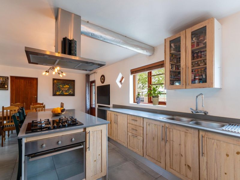Spacious kitchen featuring a central island with gas hob, built-in oven, stainless steel extractor, double sink, and ample wooden cabinetry with stone countertops.