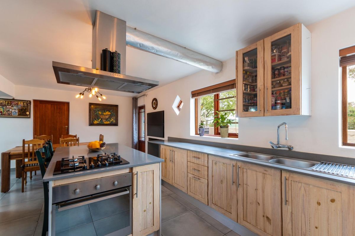 Spacious kitchen featuring a central island with gas hob, built-in oven, stainless steel extractor, double sink, and ample wooden cabinetry with stone countertops.
