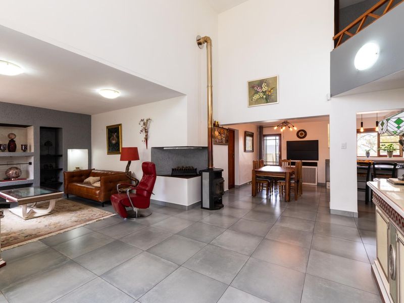 Spacious open-plan living and dining area featuring high double-volume ceilings, large format floor tiles, and a prominent freestanding fireplace.