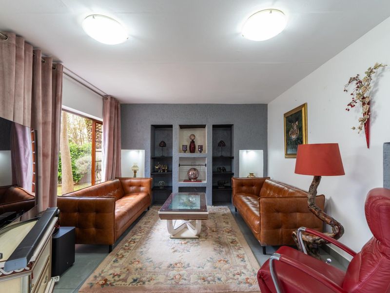 A comfortable living room featuring built-in wall shelving, recessed niches, tiled flooring, and a sliding glass door providing access to the garden.