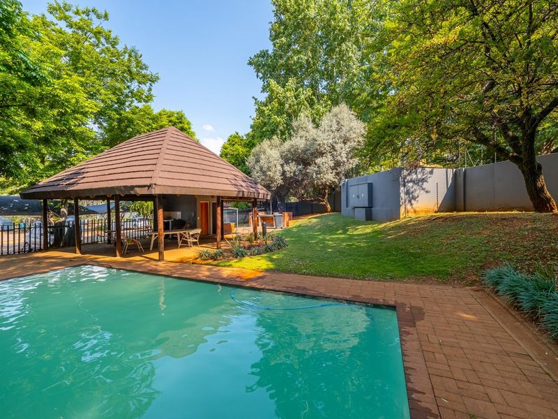 Outdoor pool area featuring a swimming pool, brick paved surround, and a covered thatched gazebo set within a landscaped garden.
