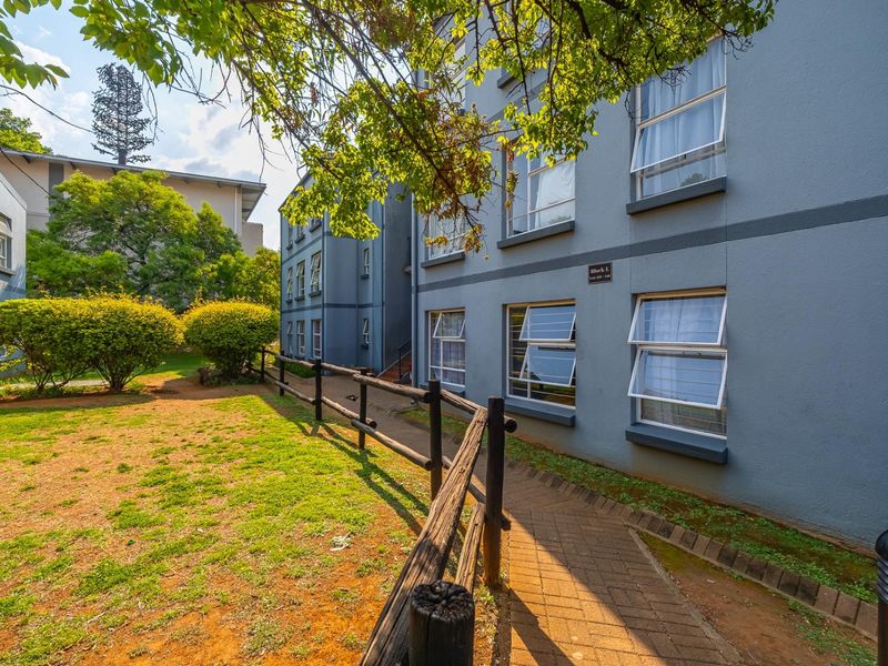 Exterior view of the apartment block featuring a paved walkway, timber fencing, and landscaped garden area.
