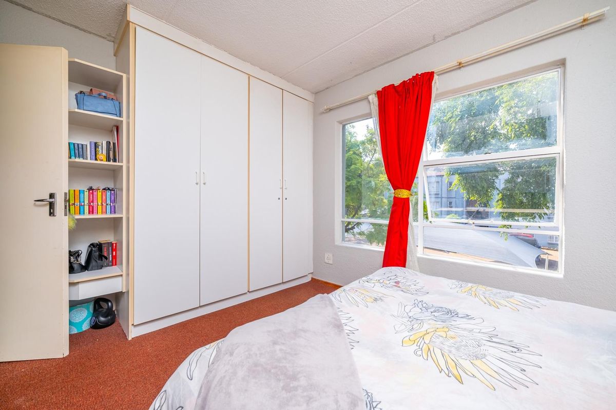 A bedroom featuring built-in wardrobes and integrated shelving, with a large window providing natural light and street views.